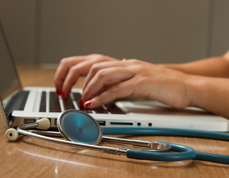 Person typing on laptop next to stethoscope